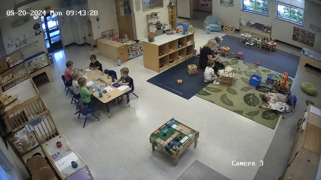 Realistic CCTV camera view of a daycare classroom with children playing, educators supervising, and activity areas visible for childcare safety, compliance, and operational monitoring.