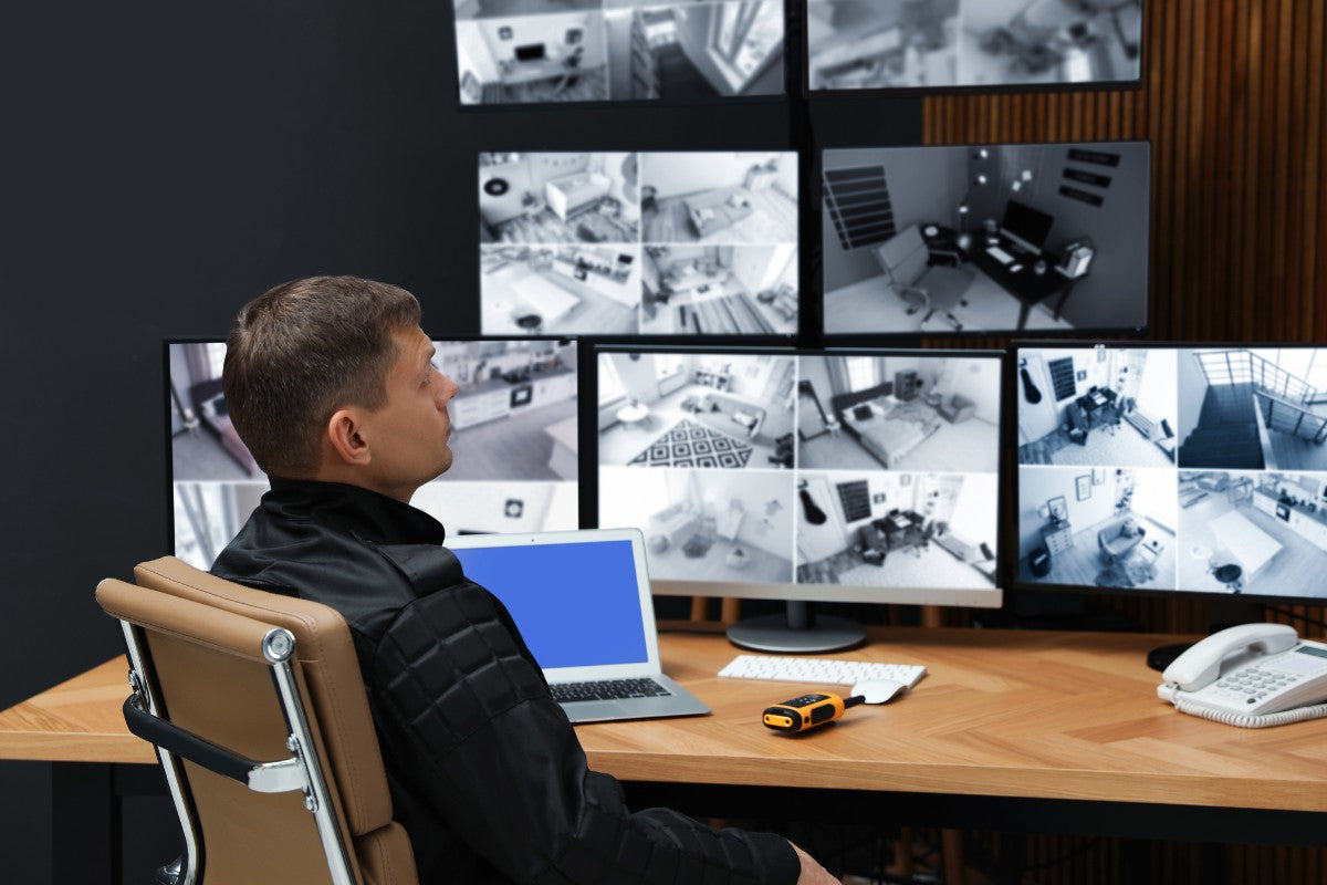 Person monitoring multiple security camera screens in a control room.
